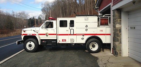 lt= A fire engine sits in front of an engine bay near a road.