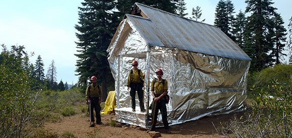 Firefighters stand near a cabin wrapped to protect it from wildfire.