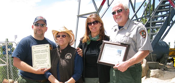 A small group of people in front of lookout tower holding a plaque.