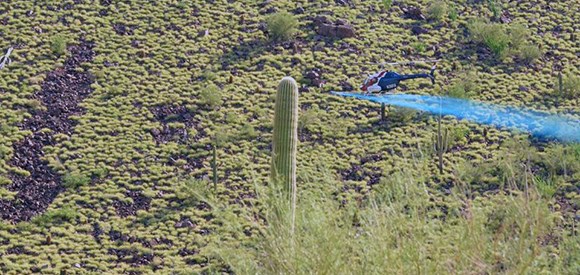 helicopter deposits a blue liquid over a hillside covered in buffelgrass.