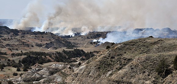 Smoke rises in multiple places from badlands.