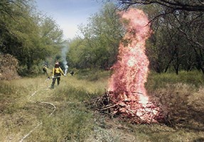 lt= A firefighter stands near a burning pile monitoring the situation.