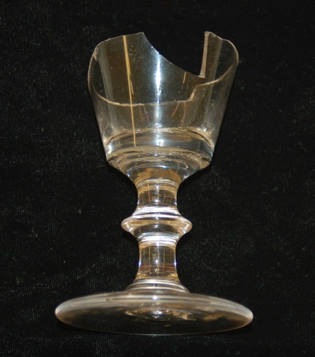 Photo of wine glass with wide base and broken rim, small size overall.