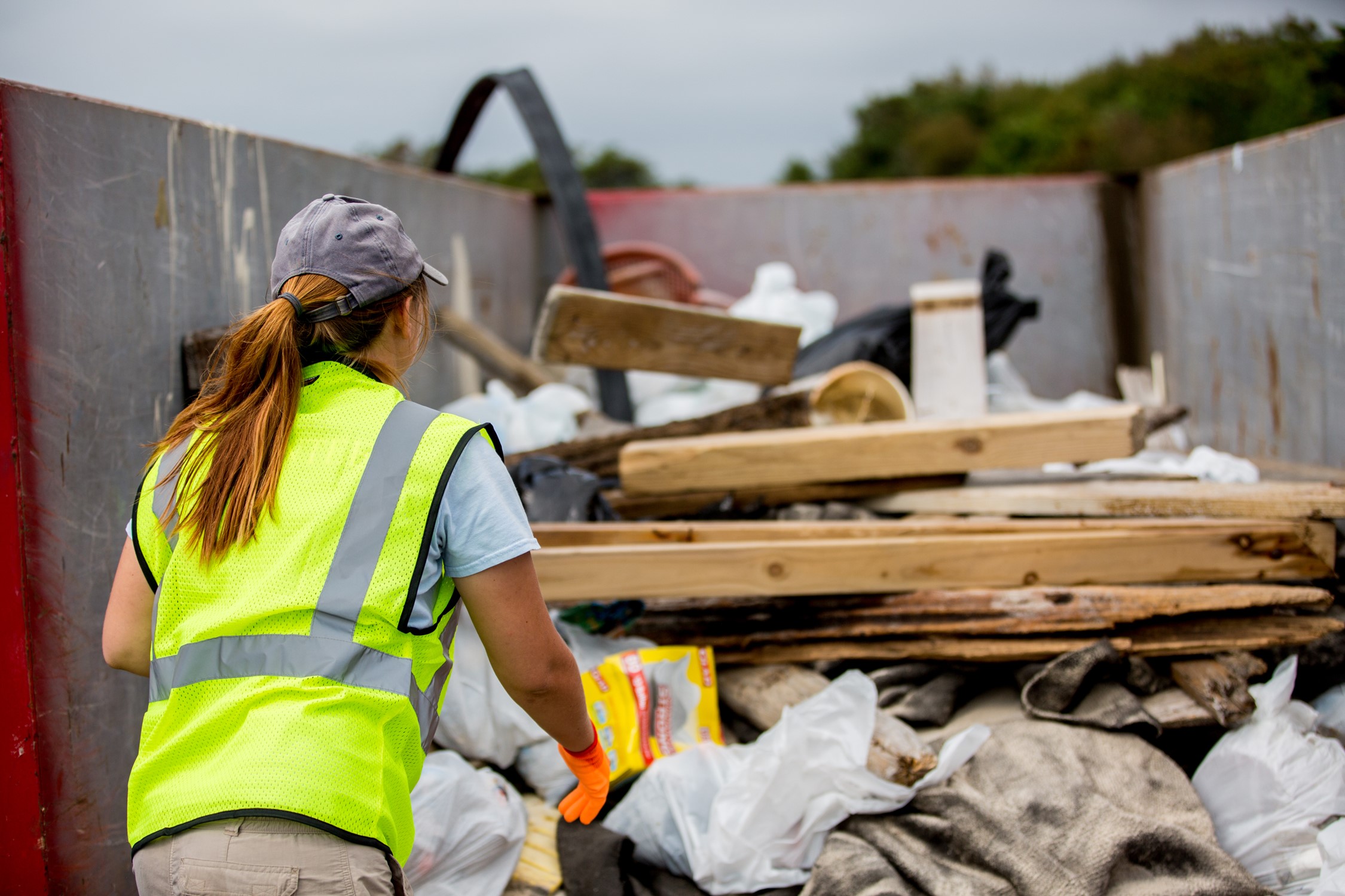 Beach Cleanup Volunteer A volunteer in a fluorescent yellow safety vest throws debris from Assateague's beach into a dumpster.