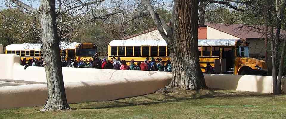 Students stand next to an adobe wall and school busses. Students stand next to an adobe wall and school busses.