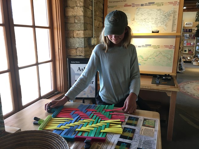 A student learning how to weave by using the interactive Artifact Kart in the visitor center.