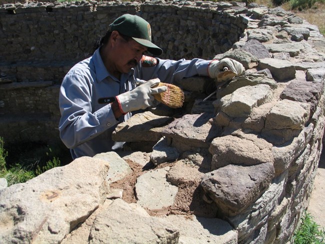 A National Park Service employee working on repairing the stone of a sandstone structure.