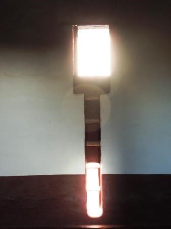 A doorway in a wall with five ladder rungs below it; the bottom section is illuminated by a narrow section of sunlight.