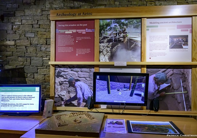 An exhibit in the museum titled "Archeology at Aztec" that details the excavation of the site, as well as the ongoing preservation. There is a 3D model of the great house on a table and a computer screen with an interactive map displayed.