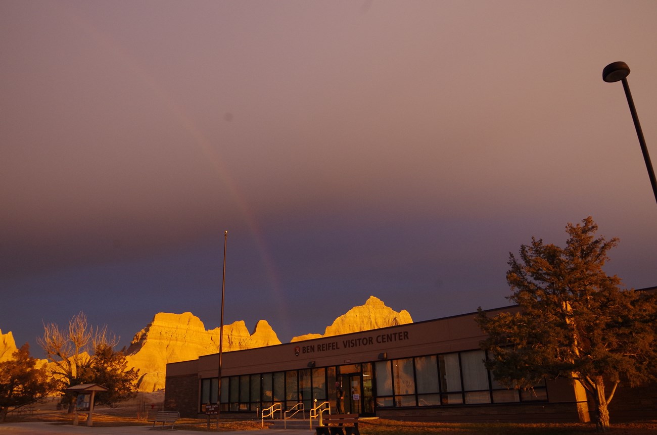 Front view of Ben Reifel Visitor Center illuminated by golden sunlight with badlands formations in background