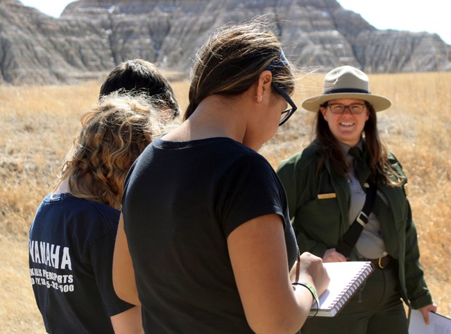 Three students work with a park ranger to make observations in a nature journal.