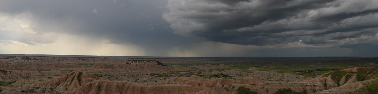 dark storm clouds and distant rain roll over sprawling badlands formations.