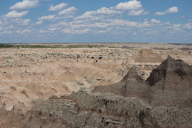 Overlook at the end of Window Trail in Badlands National Park, featuring expansive layered rock formations, eroded ridges, and deep gullies stretching to the horizon under a partly cloudy sky.