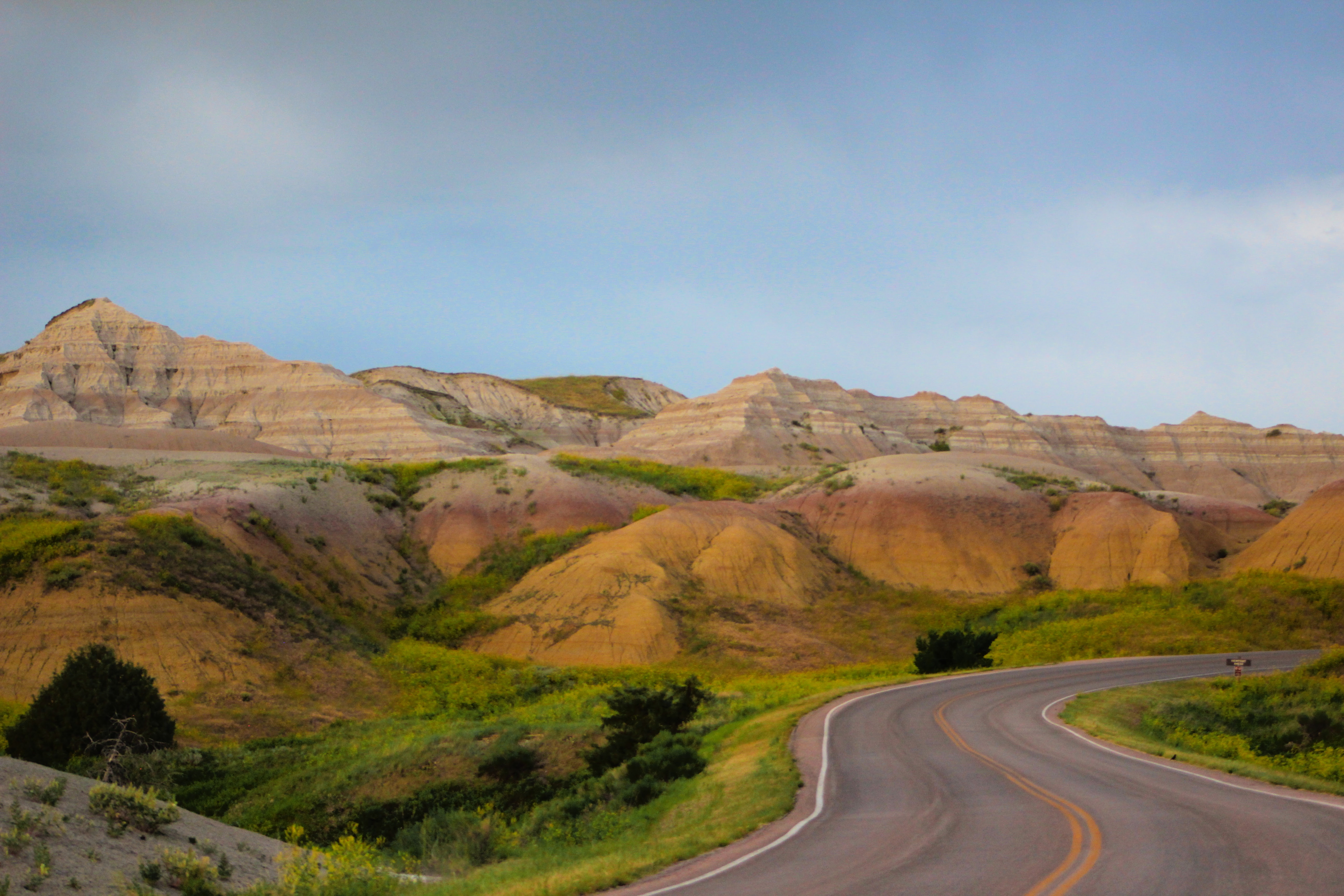 Winding road leading up to yellow mounds formations- low rolling yellow hills with a purple layer at the top.