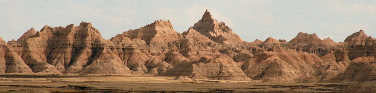 badlands_5898311661_o.jpg golden sunlight washes over the jagged peaks of badlands formations rising up and out of a dull green prairie.