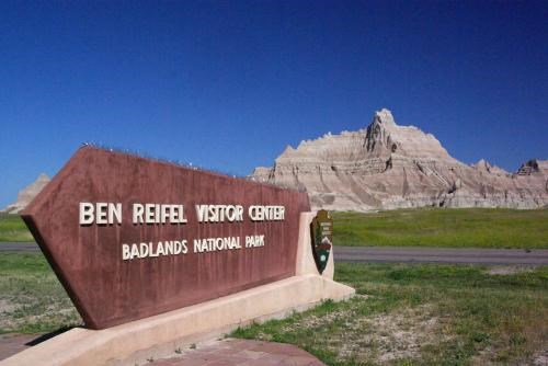 a retro brown sign reading Ben Reifel Visitor Center sits in front of banded badlands buttes.