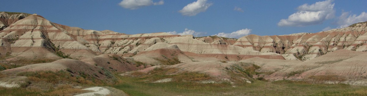 a wall of buttes with dark red stripes lie in front of a stretch of green prairie.