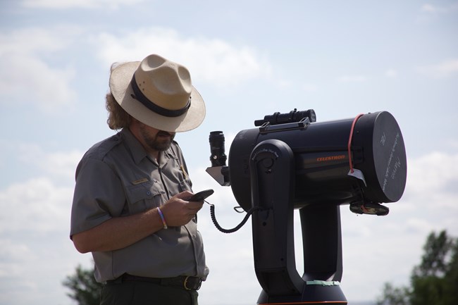 a park ranger looks down at a large telescope and uses a remote to set its angle