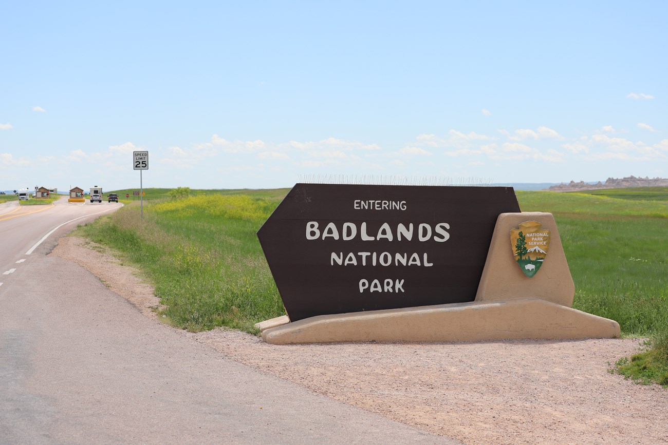 Badlands entrance sign alongside road with text "Entering Badlands National Park" under blue sky