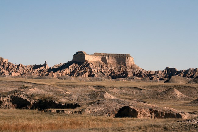 View of Stronghold Table in the South Unit of Badlands National Park: a large grassy top butte with jagged, sloped, sides.