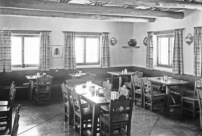 A black and white photo of a dining room. Tables and chairs are setup throughout the room.