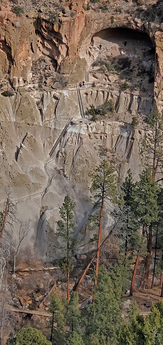 a series of ladders and stone stairs climb a steep cliff wall to an alcove