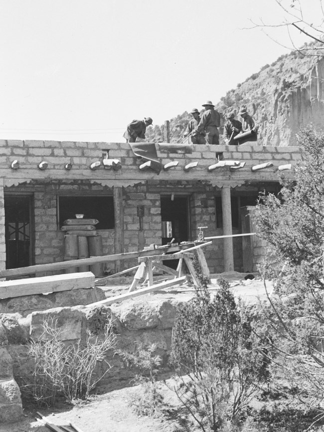 A black and white image of men standing on a roof surrounded by construction equipment.
