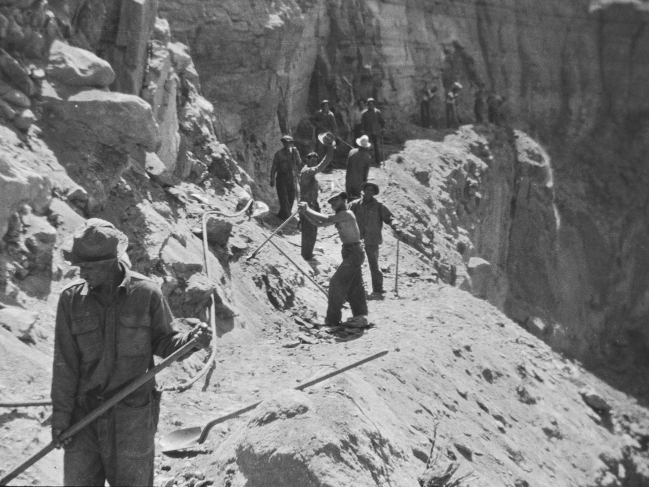 A black and white of men with tools working on a rocky trail.