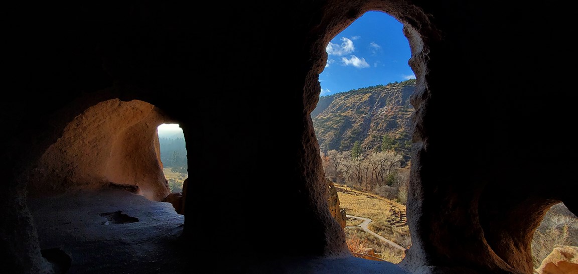 view looking out of a cavate with stone structures at the bottom of a canyon