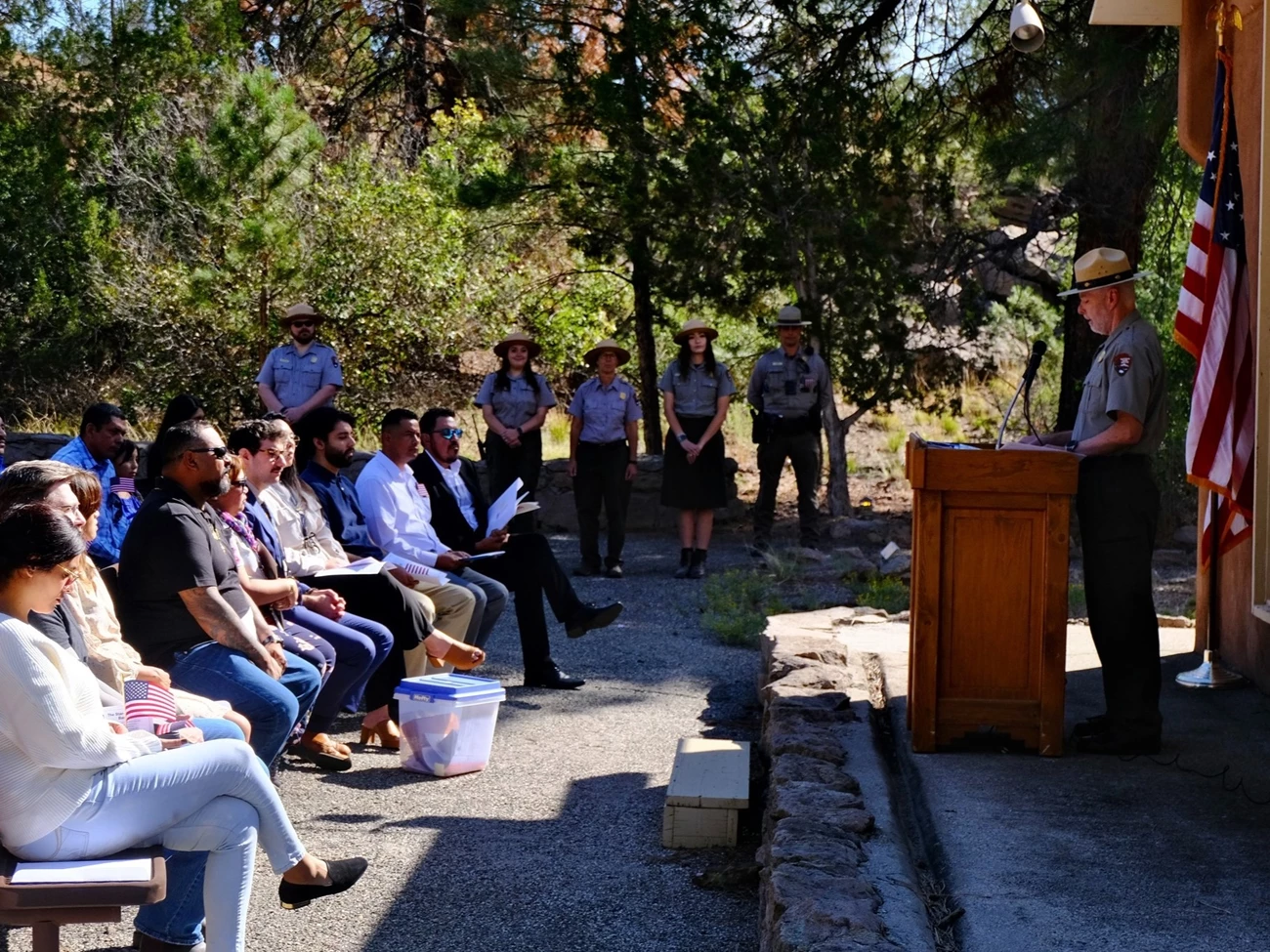 New citizens and park rangers at Bandelier's 2023 naturalization ceremony. A group of people sitting and facing a park ranger standing at a podium.