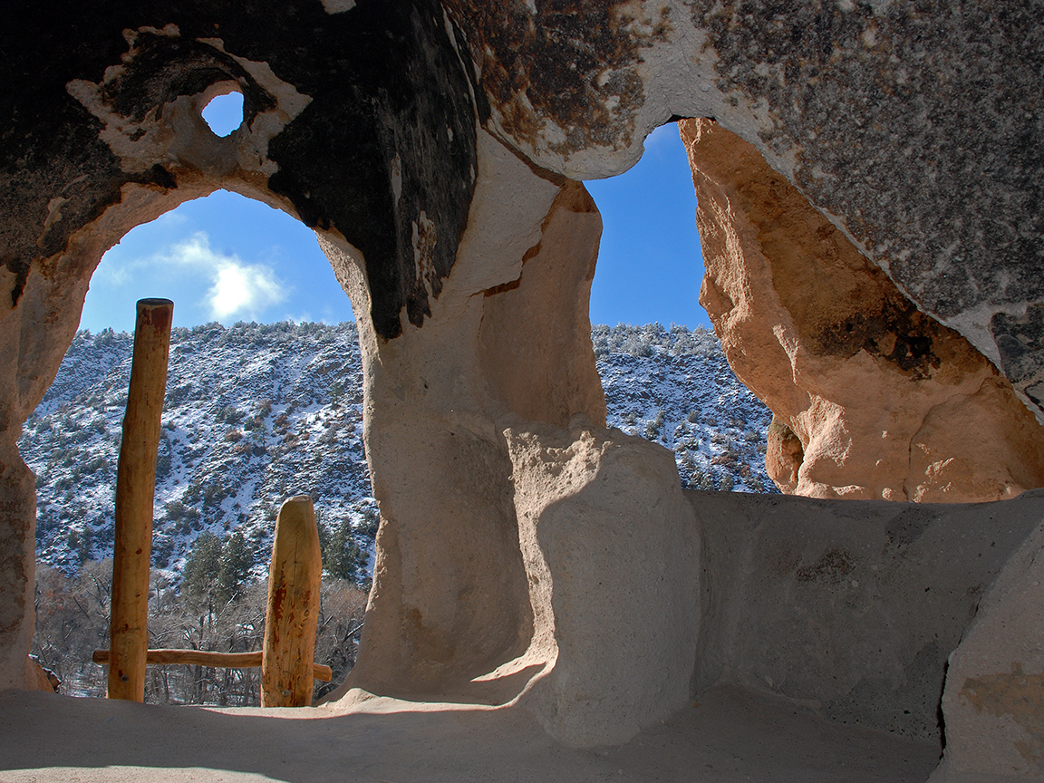 Bandelier National Monument will open at 12 noon on Friday, December 1, 2023 due to recent snowfall. A view of a white snowy canyon from inside a cliff dwelling.