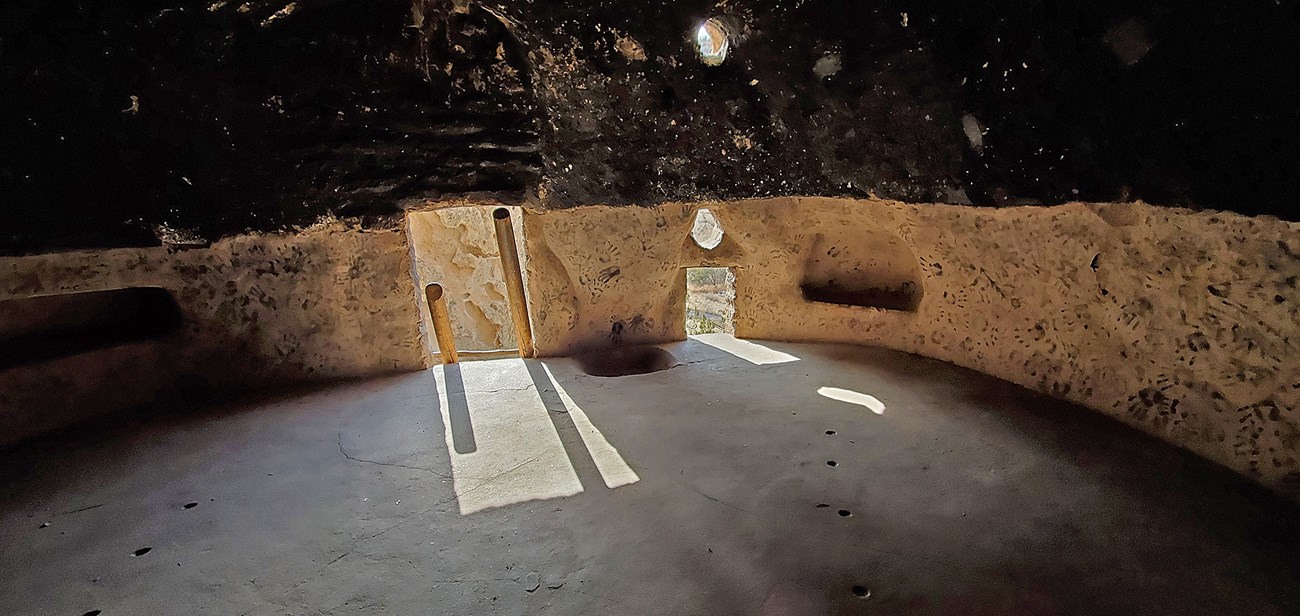 a view inside of a cavate shows a lit entrance with a darkened ceiling, pale plastered lower walls covered with dark handprints.