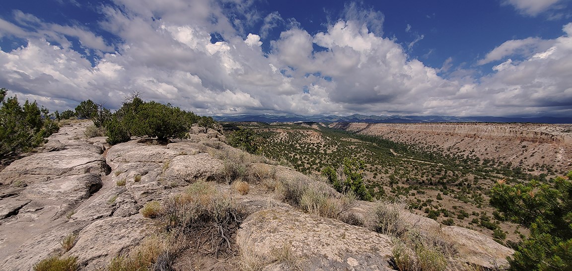 looking along a narrow mesa clouds and mountains can be seen in the distance