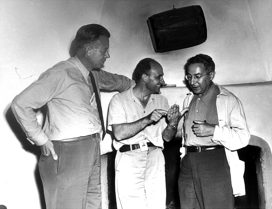 Scientists from Los Alamos frequently visited Frijoles Canyon Lodge. In this 1946 photograph Ernest Lawrence, Enrico Fermi, and I.I. Rabi stand in front of the fireplace in the lodge lobby. This lodge lobby is now the park restaurant. Three men stand and talk in front of a fireplace.