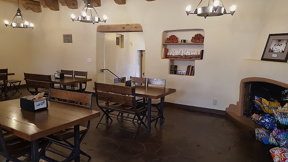 Inside a building. Tables and chairs are to the left, and a fireplace is to the right.