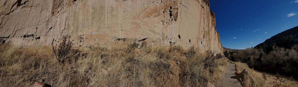 remnants of large stone structures at the base of a cliff with a narrow canyon behind