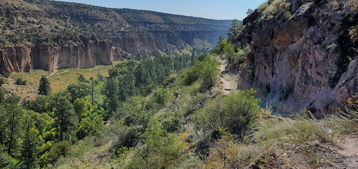 a narrow trail on the side of a canyon wall looks over archeological sites