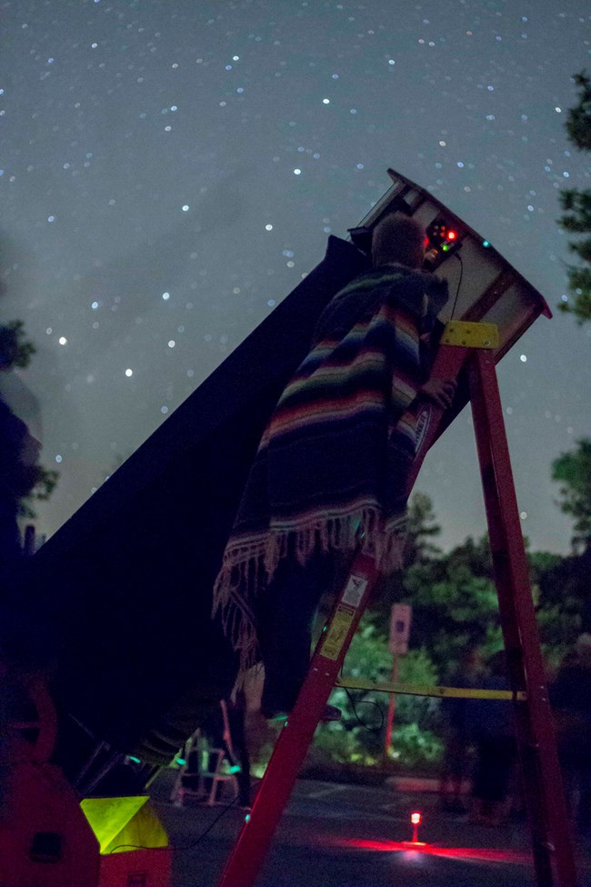Person wearing a blanket looking through telescope Person wearing a blanket looking through telescope