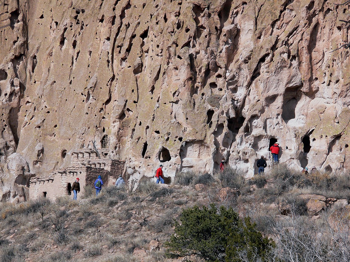 a view of a cliff face with people walking in front of it and in places climbing ladders