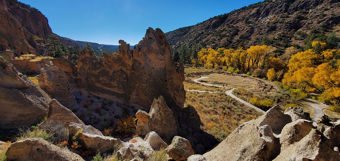 a view of a wide canyon with the remnants of many stone structures and trees with yellow leaves