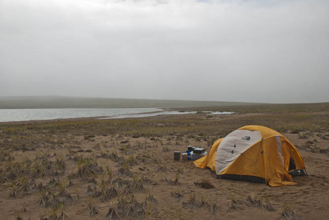 A dark storm sweeps over the lake beyond the tent