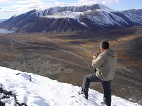 A man standing in snow on a late autumn day on the side of a mountain in Russia. He is overlooking a valley across to a mounting range on the other side. A man standing in snow on a late autumn day on the side of a mountain in Russia. He is overlooking a valley across to a mounting range on the other side.