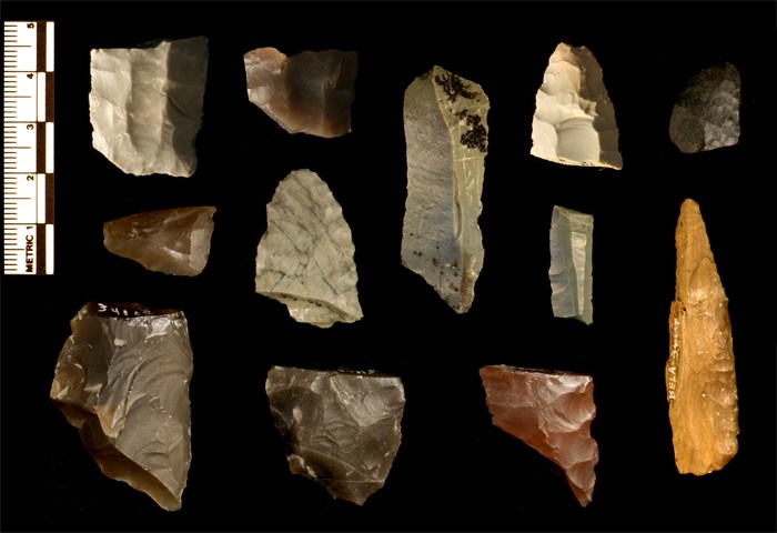 Pieces of arrowheads on a black background with a metric measurement scale on the lefthand side