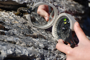 Up close view of a hand holding a brunton to a rock, a device used to measure geological features Up close view of a hand holding a brunton to a rock, a device used to measure geological features