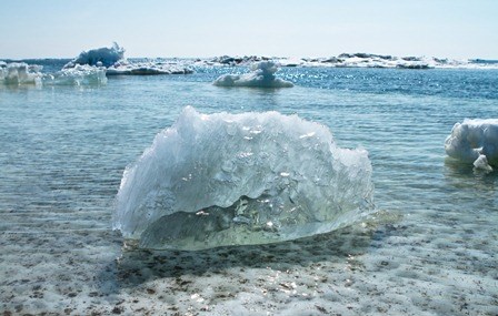 A chunk of clear ice floats in crystal clear water, with more sea ice in the background