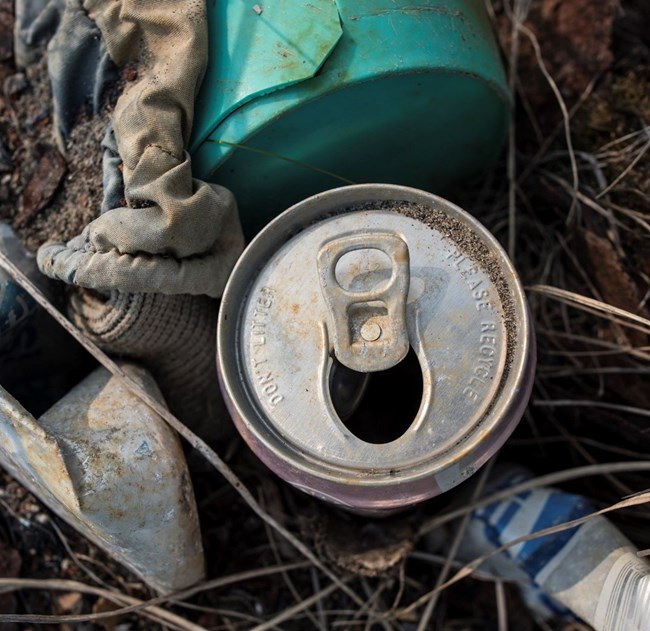 A pile of marine debris sits on the beach. In the center, an old metal can has the words, "Don't litter, please recycle," printed on the top.