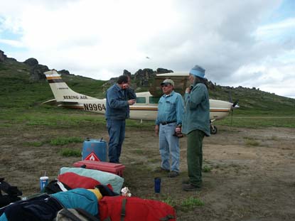 Three men with camping gear standing near a small airplane Three men with camping gear standing near a small airplane