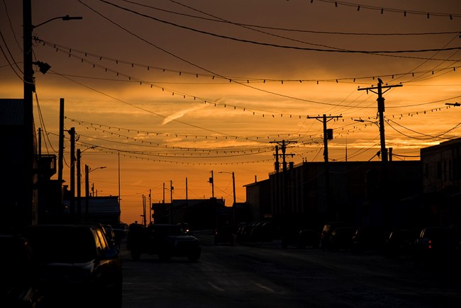 The sun rises behind a street lined with buildings