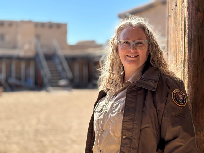 Adult woman in volunteer shirt and jacket welcomes fort visitors at door