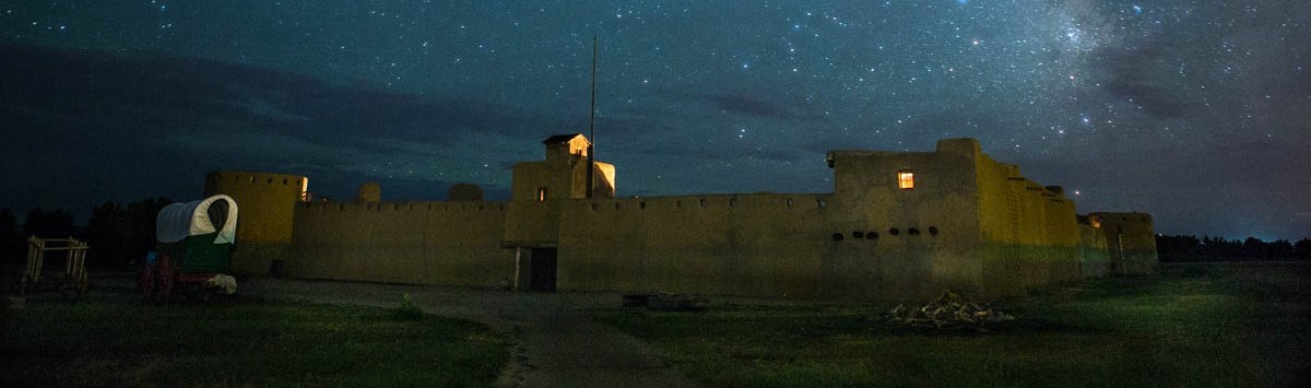 A large walled adobe structure is seen at night with stars in the sky